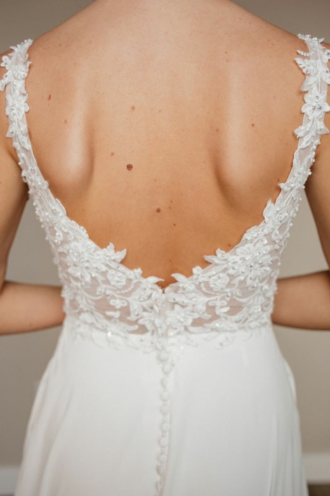 Robe de mariée «Posie» de chez Evelyne Bridal. Cette robe de mariée est en dentelle sur le buste et en mousseline sur la jupe. Une traine magnifique en dentelle avec une chute de boutons entière. Cette robe de mariée est disponible dans votre boutique Rêve d'un Jour à Yvetôt