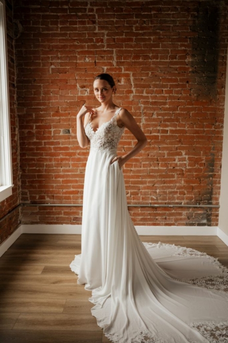 Robe de mariée «Posie» de chez Evelyne Bridal. Cette robe de mariée est en dentelle sur le buste et en mousseline sur la jupe. Une traine magnifique en dentelle avec une chute de boutons entière. Cette robe de mariée est disponible dans votre boutique Rêve d'un Jour à Yvetôt